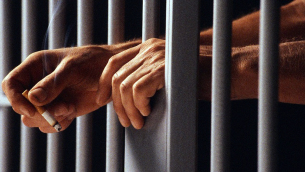 Prisoner Holding Cigarette Between Bars