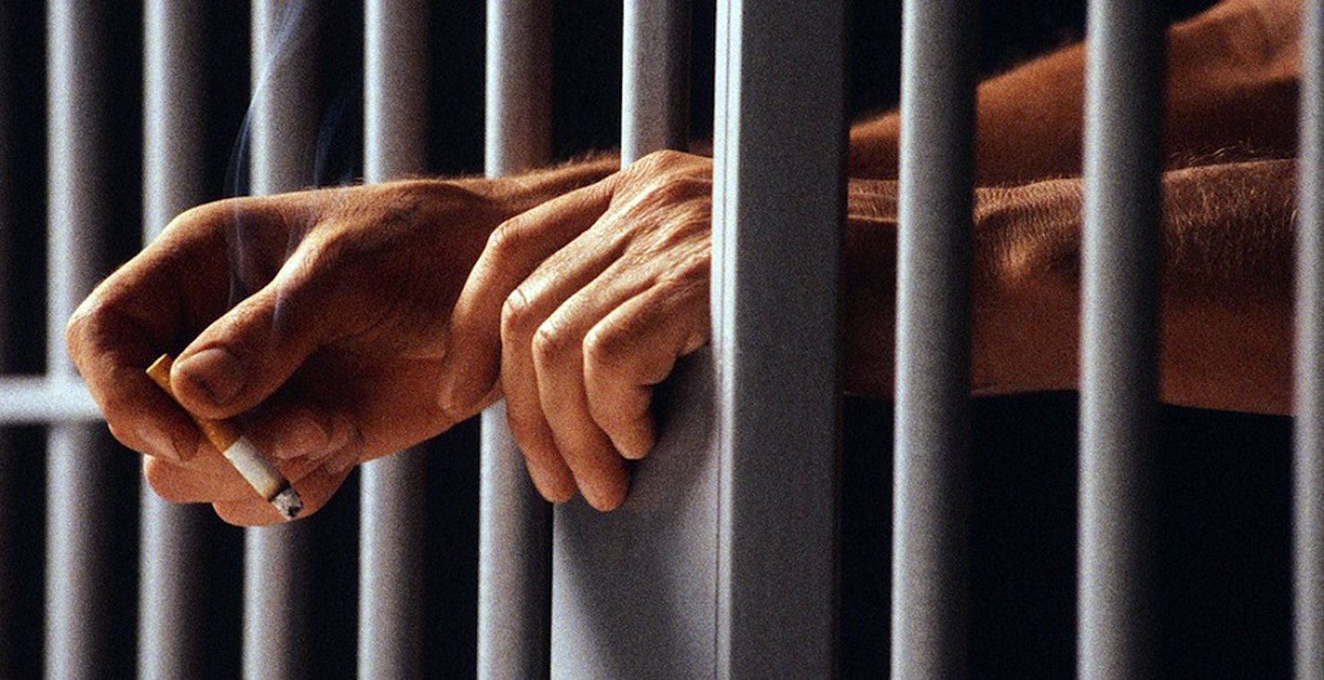 Prisoner Holding Cigarette Between Bars