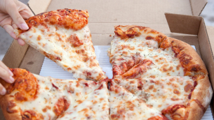 A child's hand grabbing a slice of pizza from a cardboard box.