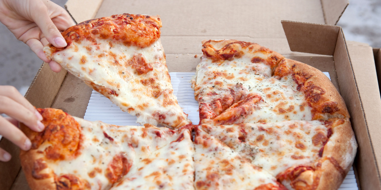 A child's hand grabbing a slice of pizza from a cardboard box.